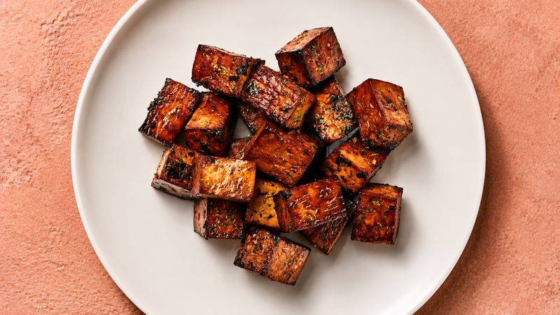 Glossy caramelized cubes of marinated tofu on a white plate.