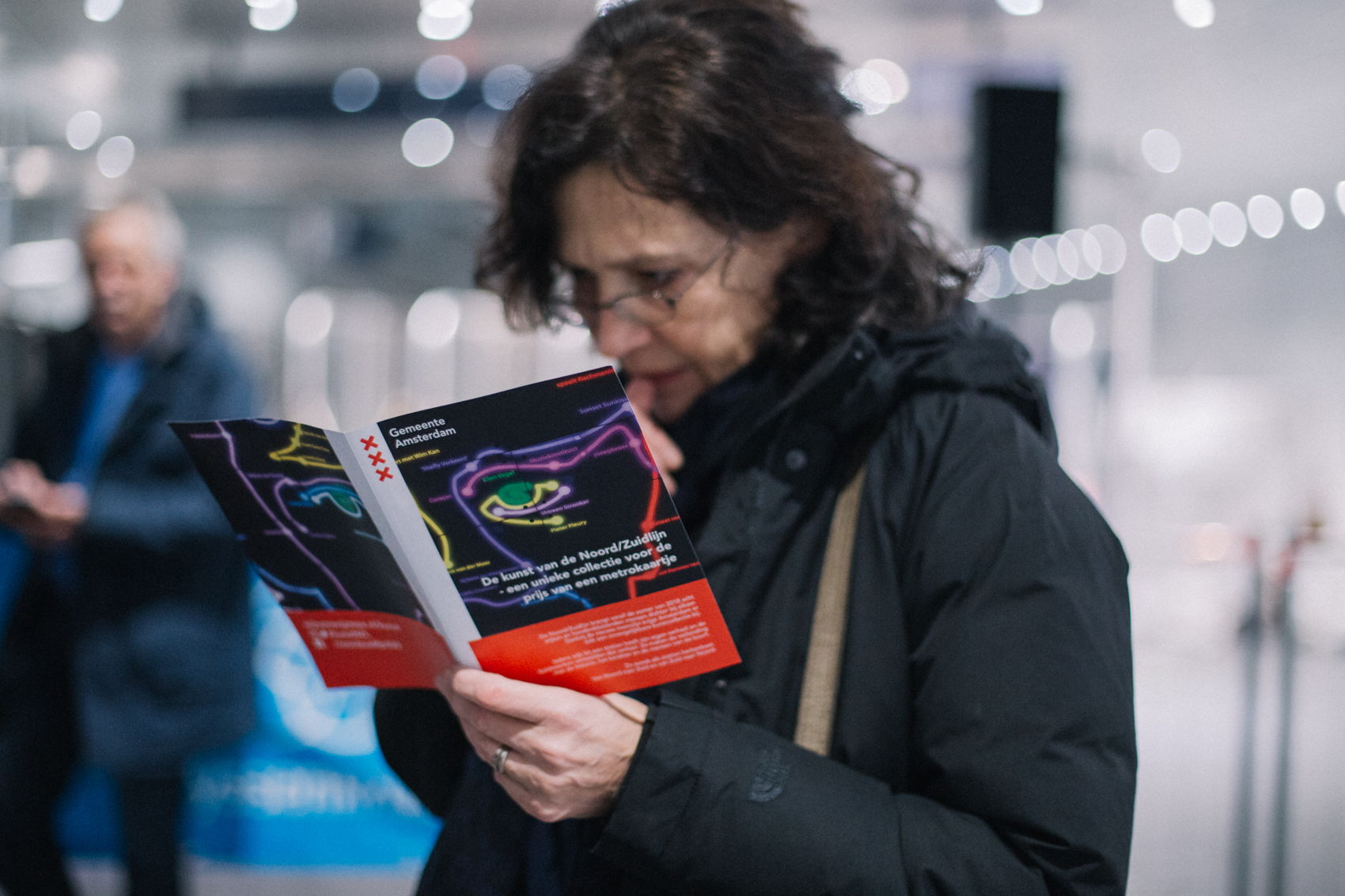 Een bezoeker van de opening van het kunstwerk in station Vijzelgracht, die de eerst gemaakte flyer over de kunstwerken in handen heeft. Foto: Nina Albeda Jelgersma Een bezoeker van de opening van het kunstwerk in station Vijzelgracht, die de eerst gemaakte flyer over de kunstwerken in handen heeft. Foto: Nina Albeda Jelgersma