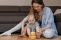 Mother and baby sitting on the floor and playing with a Montessori stacking toy. 