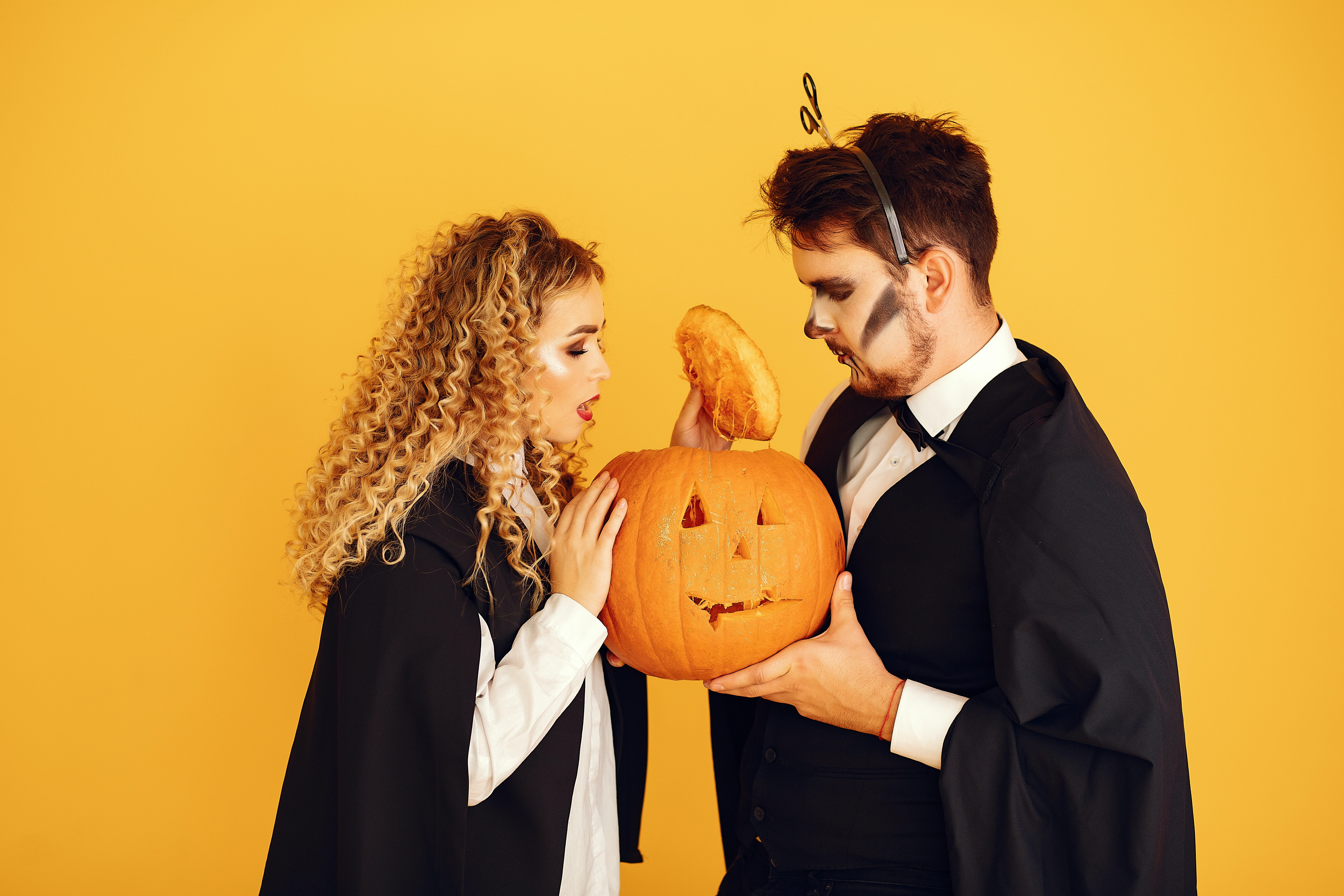 An attractive man and woman wearing vampire costumes look inside a pumpkin.