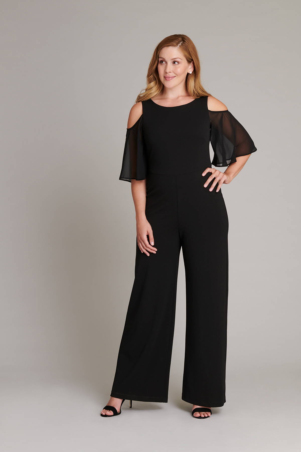 woman posing in black full-length connected apparel jumpsuit with could shoulders and chiffon short sleeves