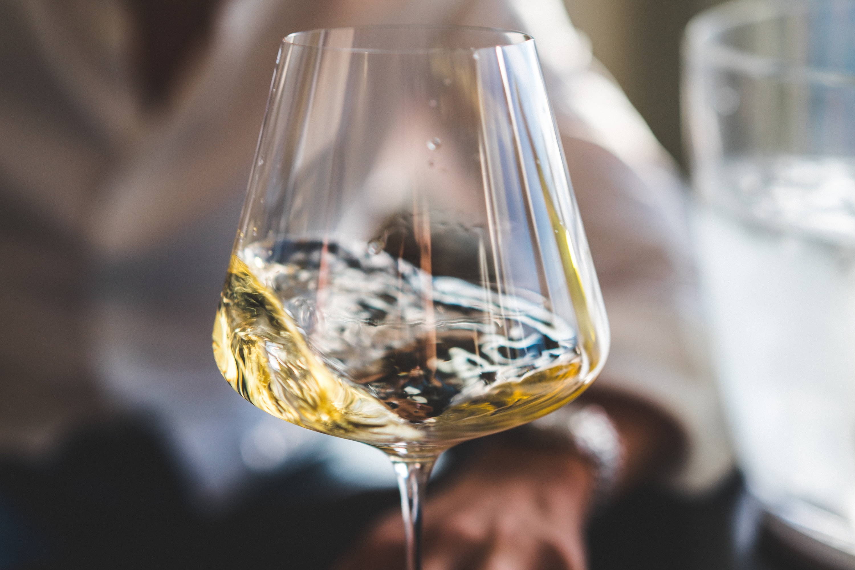 Swirling glass of white wine showing the perks of ordering wine at a restaurant by the glass. 
