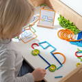 A hand placing colorful wooden sticks to create a design illustrated on a playing card featured in the Montessori Smart Sticks. 