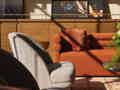 Gemütlicher Wohnbereich mit orangefarbenem Sofa, grauem Sessel, Holzregalen mit Fotos und einem gemusterten Teppich im Sonnenlicht.