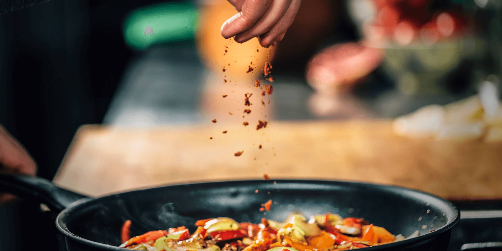 Person sprinkling spices into a sizzling pan.