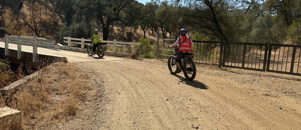 two people crossing a bridge on a dirt road on aventon aventure electric bike while on a tour with Yosemite E-Biking (yosemiteebiking.com)