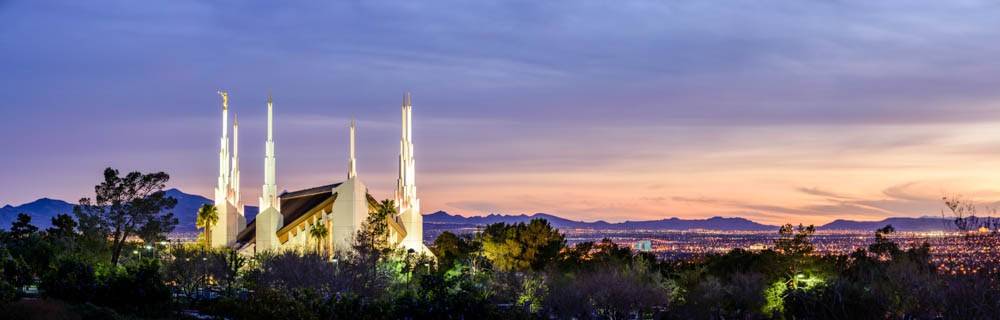 Panoramic photo of the Las Vegas Temple glowing above the surrounding trees and city. 