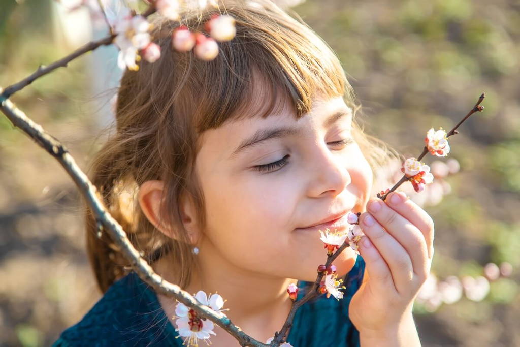 Petite fille sentant une fleur sur une branche.