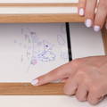 Woman's hand pointing at a magnet on the Montessori Keepsake Frame which ensures drawings are safely closed behind a featured drawing. 