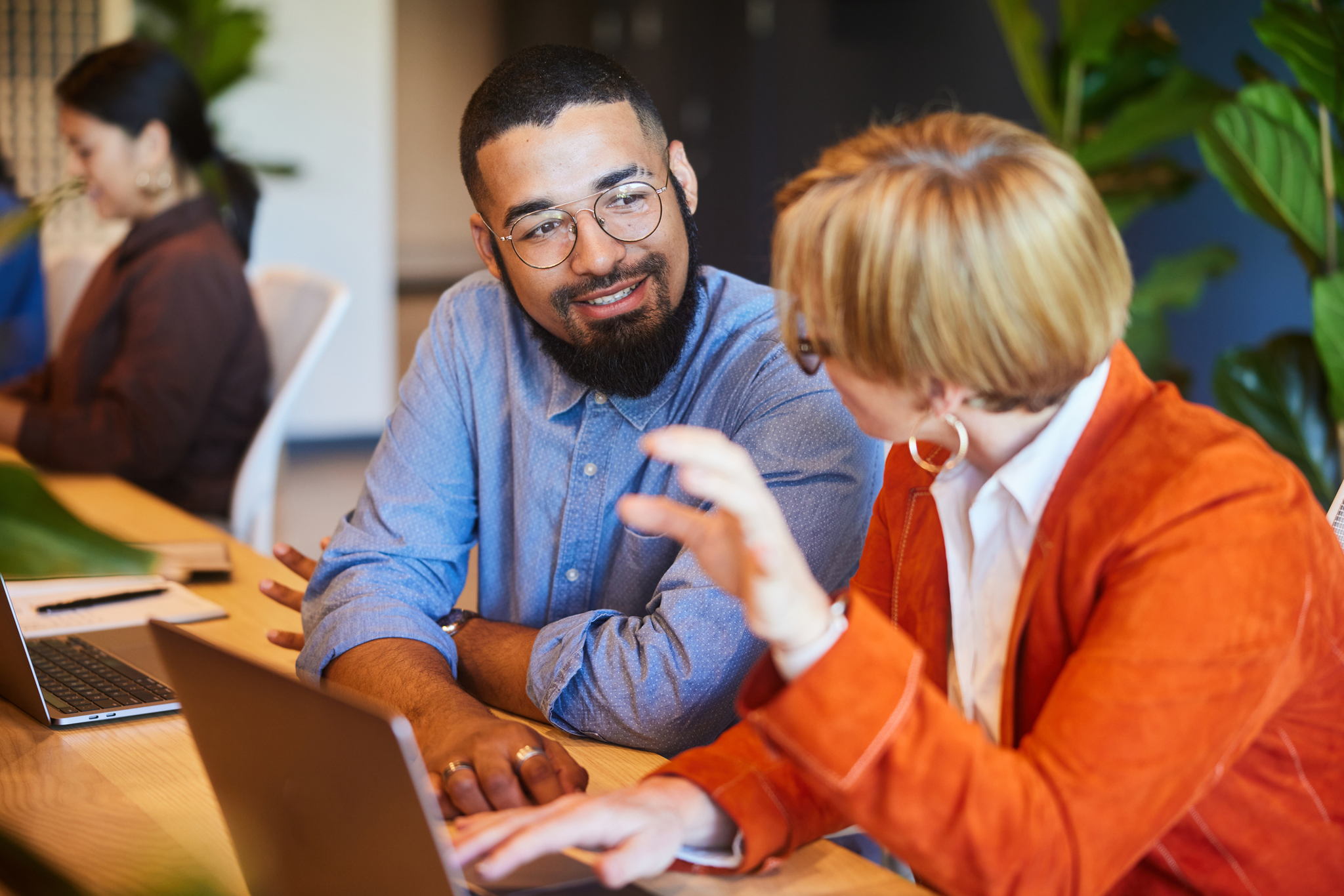 Two diverse businesspeople smiling and talking together while working at a desk in a modern office space