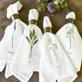 Four white napkins adorned with different flowers lay next to each other with napkin rings at the end of each 