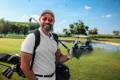 A smiling golfer standing on the green with his golf bag and golf cart.