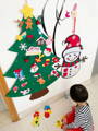 Little girl placing decorations on felt Montessori Snowman and Christmas Tree which are hanging from the wall. 