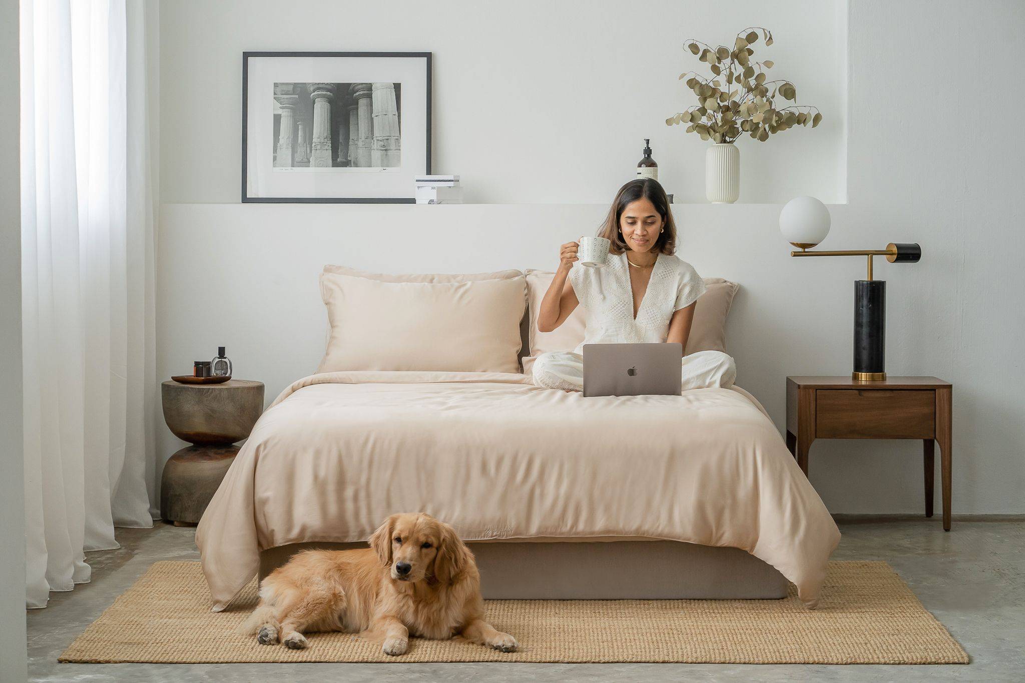 Woman working while sitting on bed featuring Weavve's Tencel Lyocell bed sheets in cream colour