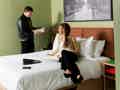 Modernes Hotelzimmer mit Kingsize-Bett, hellgrünen Wänden, Stadtbild-Kunst und zwei Personen im Raum.