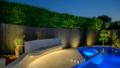 Backyard pool and curved outdoor seating area with LED strip lighting and garden spike lights illuminating trees and fence.