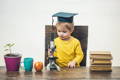 Little boy with an academic hat holding a microscope.