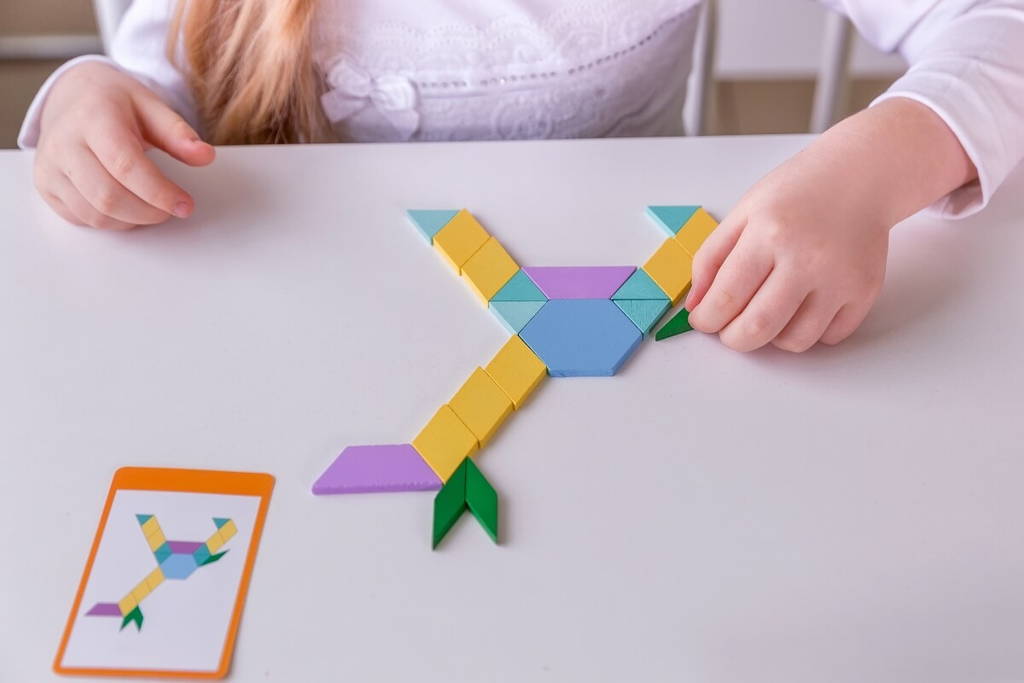 Une fille joue avec des blocs Tangram en bois colorés.