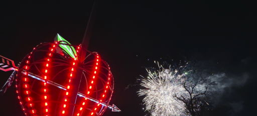 A large apple structure with red lights in the foreground, fireworks in the background, capturing a festive celebration.