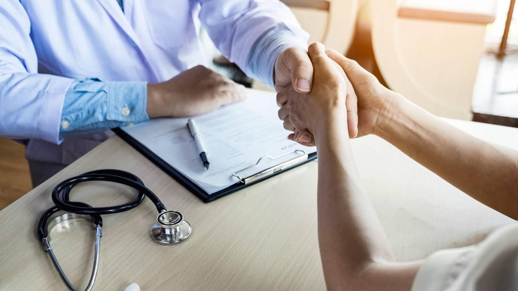 Doctor shakes hands at medical office with patient, wearing glas