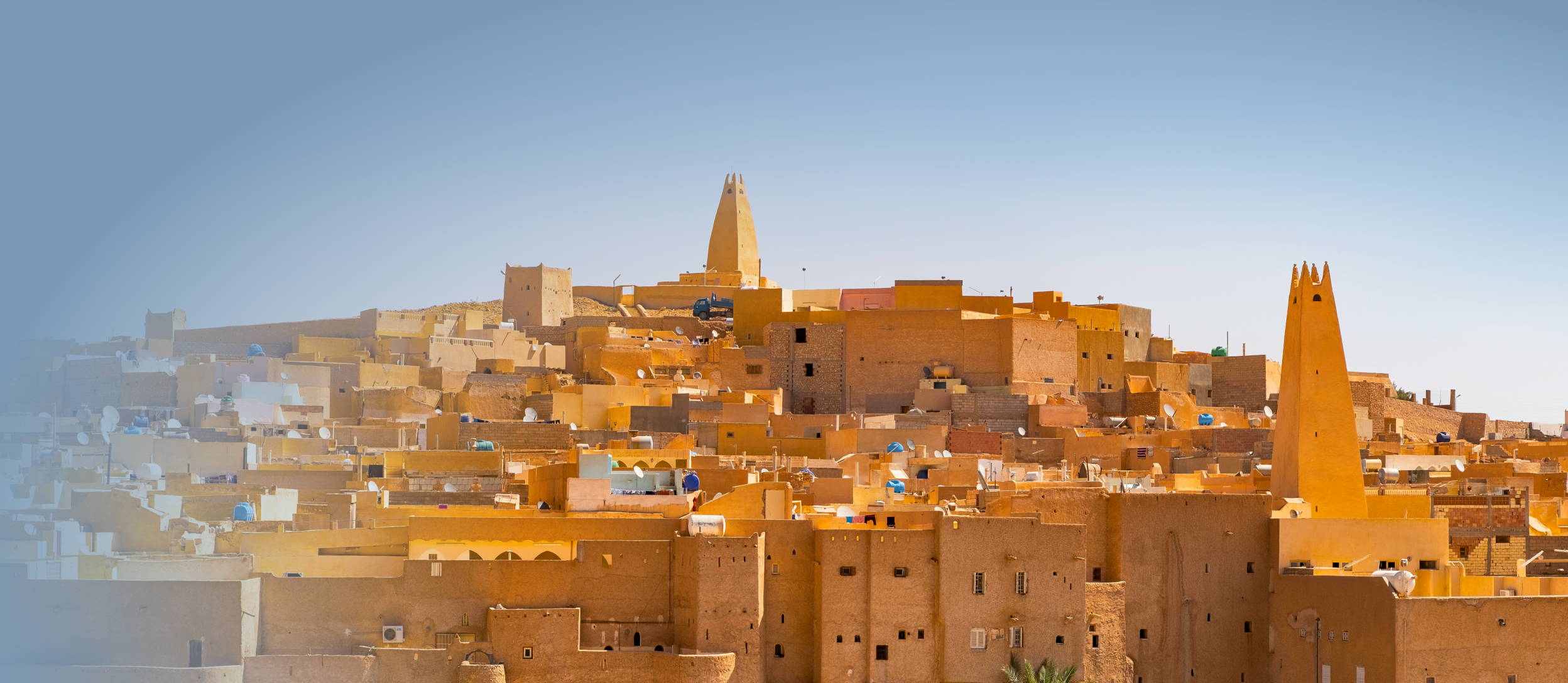 A town on a hillside, with matching tan buildings & rooftops, all getting higher into the clear blue sky. 