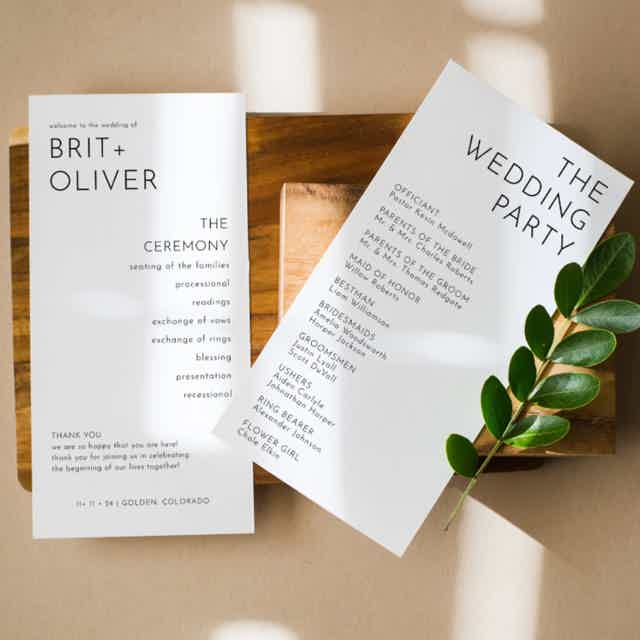 Modern wedding program with sleek sans serif font. Displayed on polished wood with lush greenery for an elegant touch