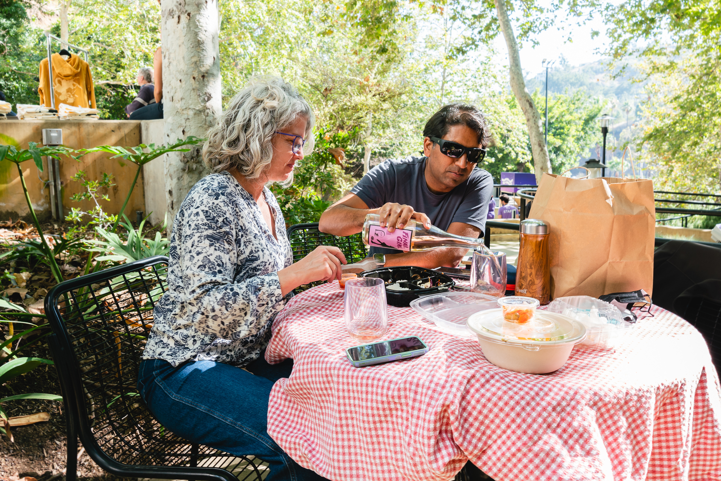 2 picnickers in the sun enjoying a bite to eat and wine before a show, in the Edison Plaza outside of the amphitheater. 