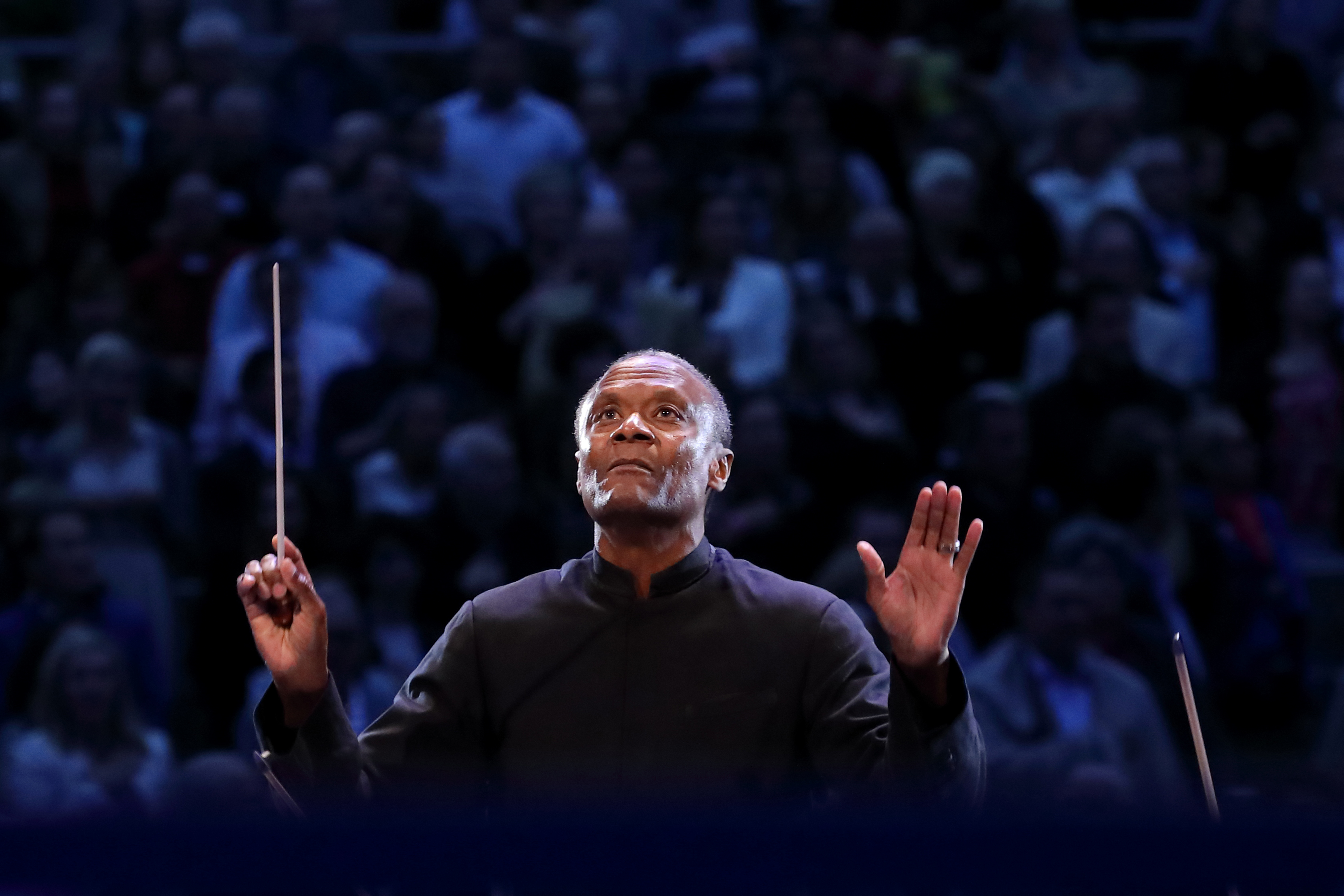 Thomas on stage, conducting and looking up at the orchestra - background blurred