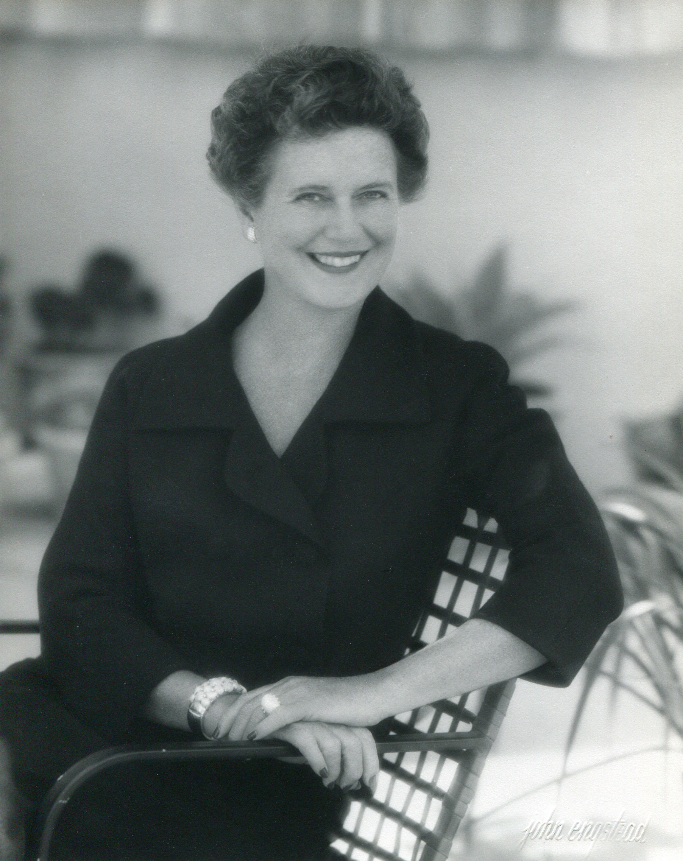 A black and white portrait of Dorothy Chandler seated outdoors, smiling at the camera.