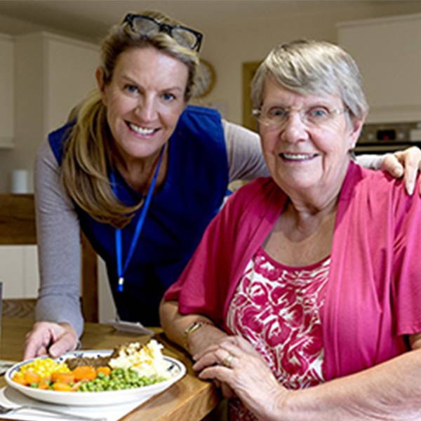 A woman sitting with an older woman delivering her a meal