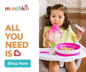 An adorable infant in a high chair, happily eating baby food with a spoon.