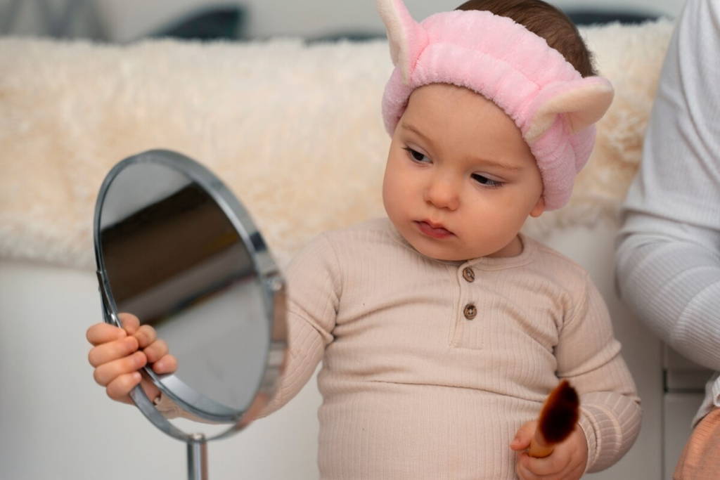 Baby girl holding a mirror in her right hand and looking at it.