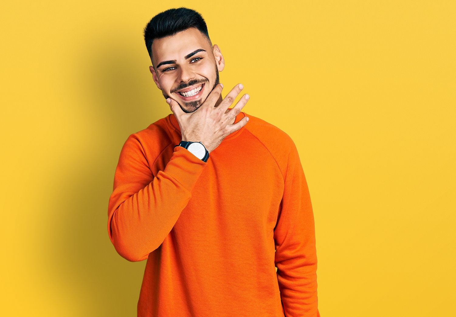 Hispanic man with beard looking confident at the camera smiling with crossed arms and hand raised on chin.