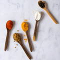 Five small wooden spoons filled with various ground spices