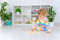 Little blonde girl sitting on the floor and playing with a puzzle. 