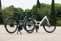 Deux vélos électriques sur un trottoir devant des arbustes verts