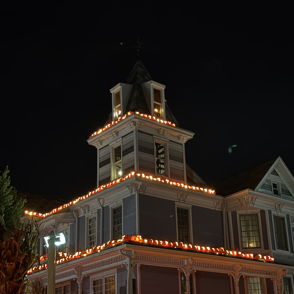 A lit house with orange Halloween lights and grinning pumpkins creates a warm, festive atmosphere full of joy and nostalgia.