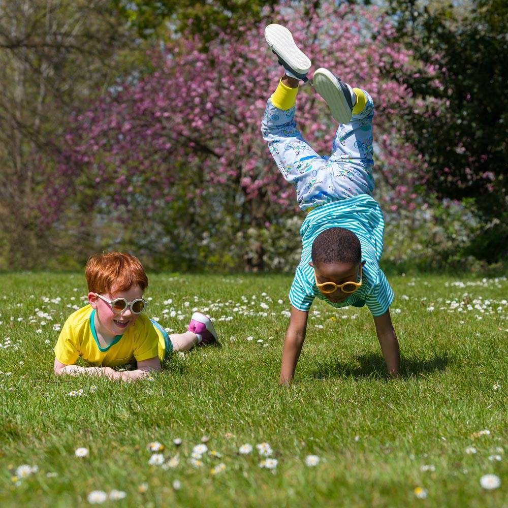 Image of two happy children playing in the park. One boy is doing a handstand. The other is lying in daisies. Both are wearing bright, colourful Ducky Zebra clothes