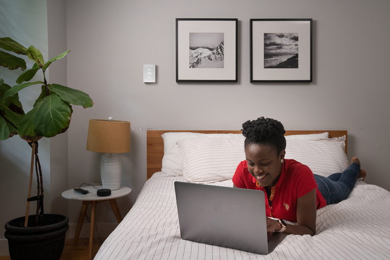 woman smiling and laying on her bed while on her laptop