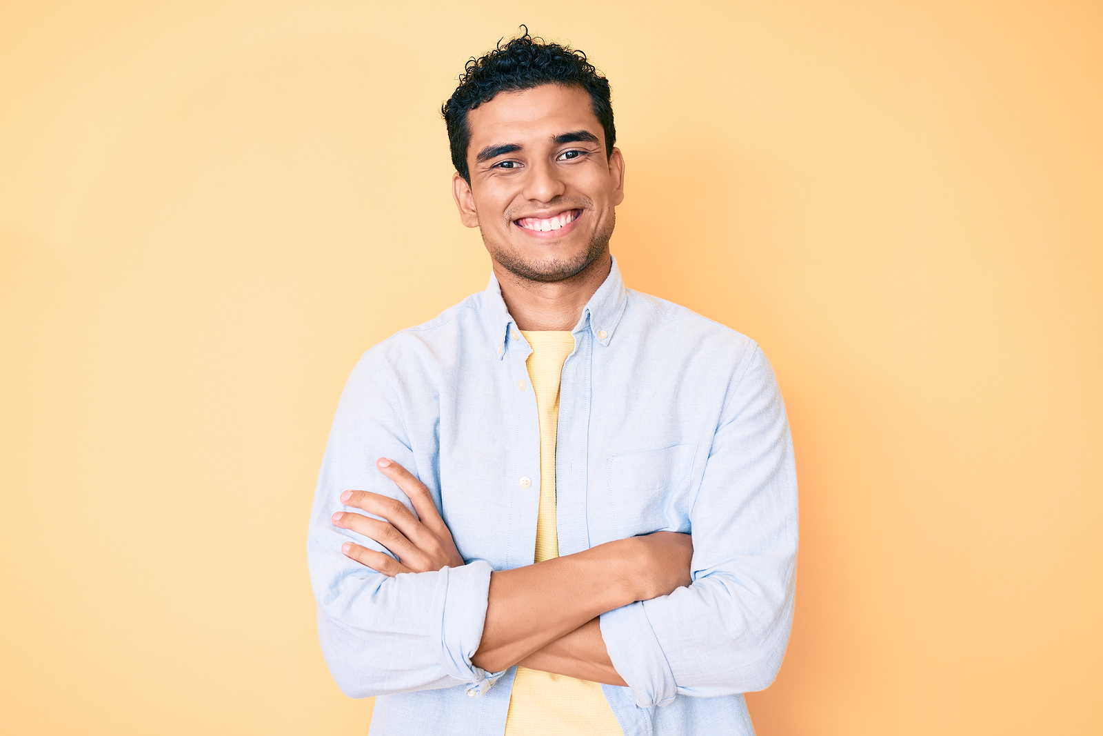 A young latino man stands with arms crossed and smiles.