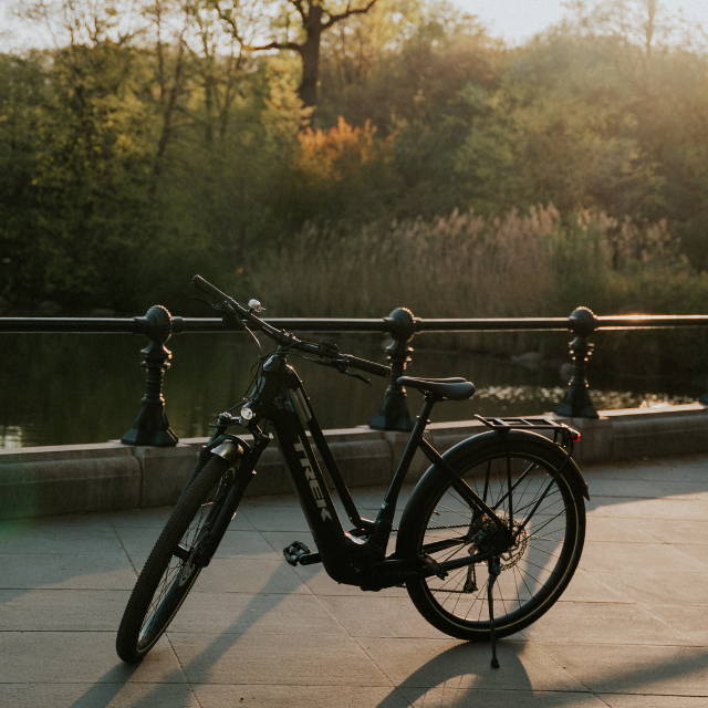 a black Trek Allant electric city bike on a bike path by a body of water