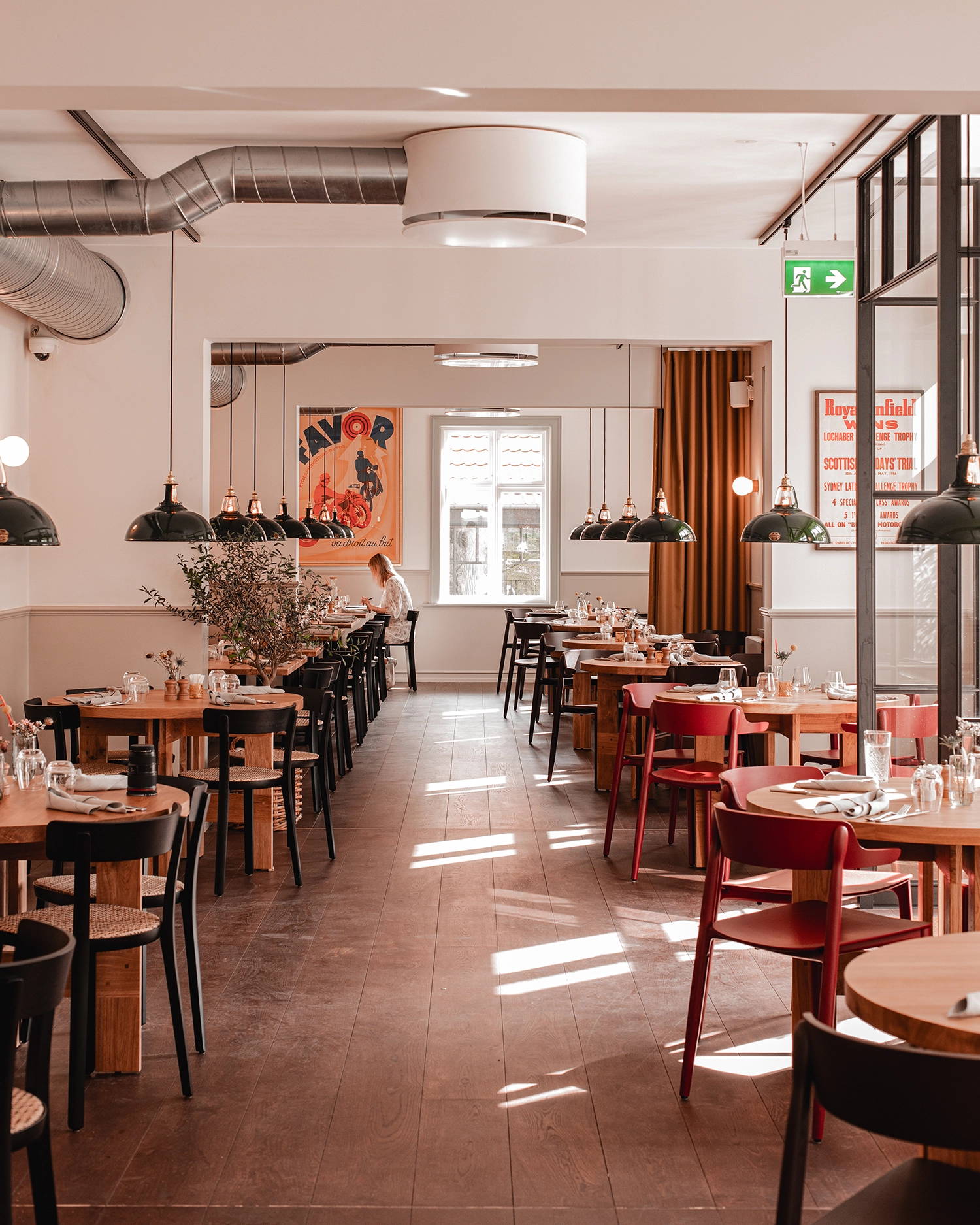 Looking down a Scandinavian restaurant at two rows of tables with Large Green Coolicon lampshades hanging above each one. 
