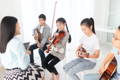 A group of young children holding stringed instruments participating in a group music lesson with their instructor.