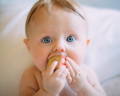 Blue eyed baby putting a wooden cube toy in its mouth. 