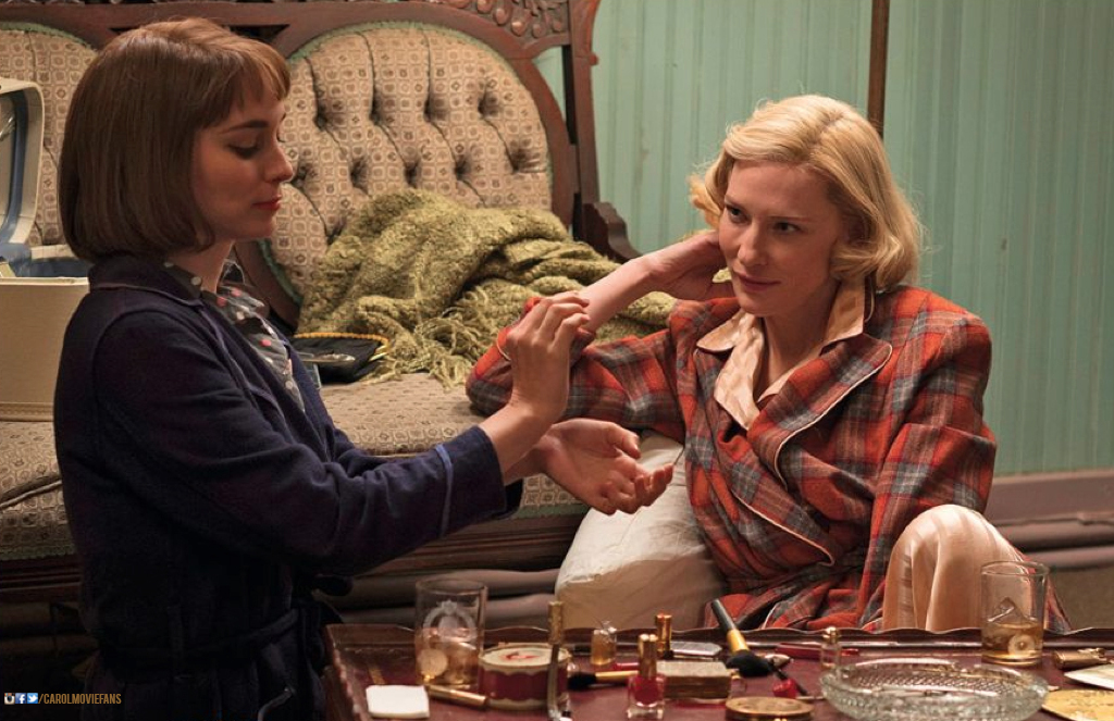 Carol watching Therese as she tries on a perfume on her wrists.