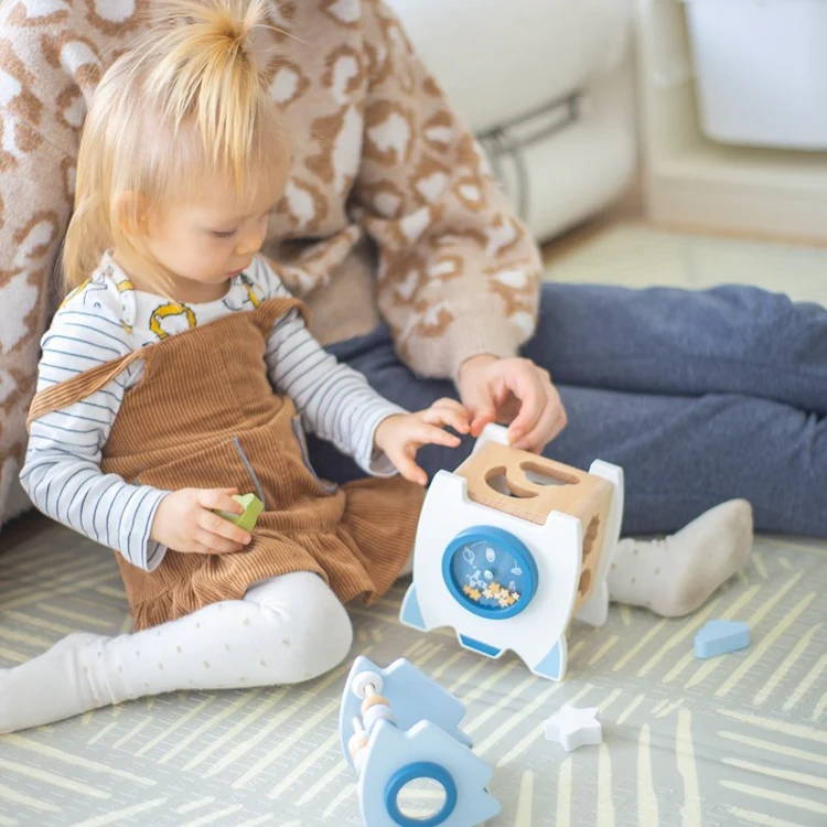 Little girl taking the top of the Montessori Learning Rocket wooden toy.