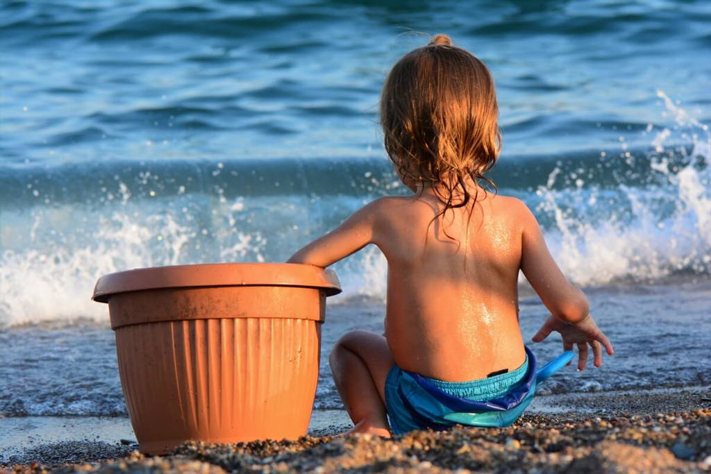 Toddler enjoying at the beach and looking at an upcoming wave.