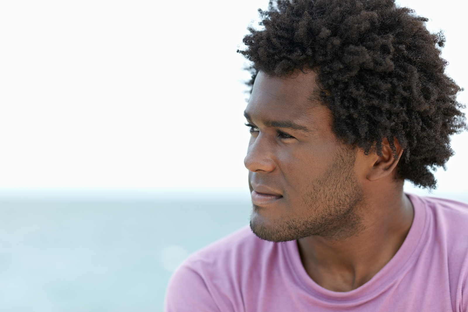 A multi ethnic man looking into the distance wearing a purple shirt and he has an afro.