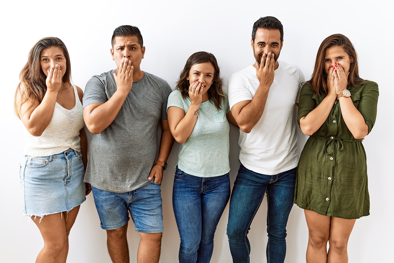 Group of young friends standing together over isolated background laughing and embarrassed giggle covering mouth with hands.