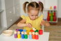 Little girl playing with colorful Montessori wooden pegs.